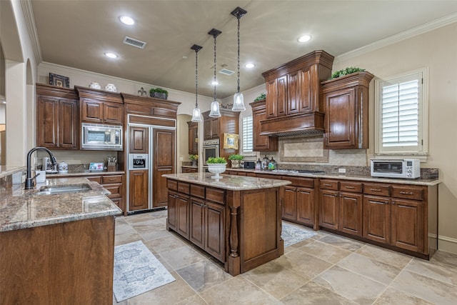 kitchen with visible vents, pendant lighting, built in appliances, light stone countertops, and a sink