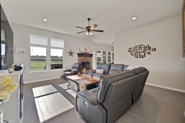 living room with a brick fireplace, a ceiling fan, baseboards, recessed lighting, and wood finished floors