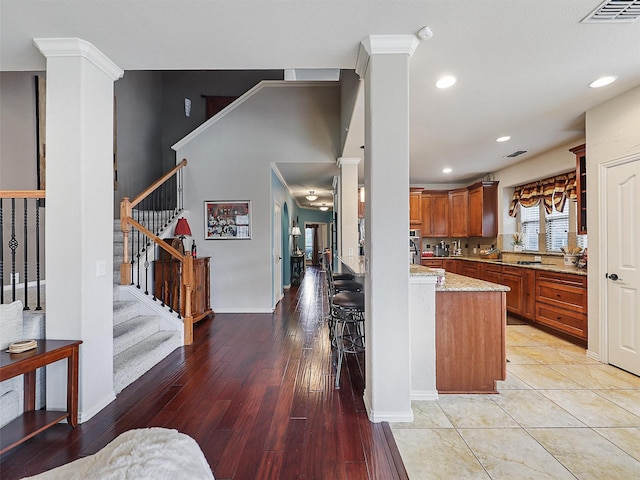2420 Forest Gate Dr, Little Elm, TX 75068 - kitchen featuring ornate columns, brown cabinets, light stone countertops, a peninsula, and light wood-type flooring