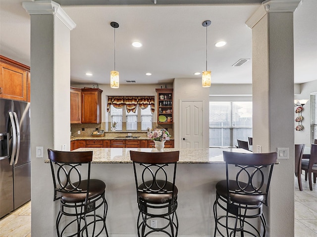 2420 Forest Gate Dr, Little Elm, TX 75068 - kitchen with stainless steel fridge with ice dispenser, brown cabinets, decorative columns, plenty of natural light, and recessed lighting