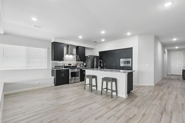 1036 Fairfax Dr, Godley, TX 76044 - kitchen with appliances with stainless steel finishes, wall chimney exhaust hood, dark cabinets, a breakfast bar, and light wood-style flooring
