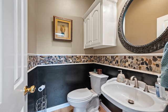 bathroom with toilet, a sink, and a wainscoted wall