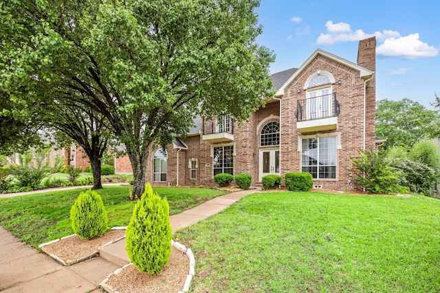 traditional-style house featuring french doors, a front yard, a balcony, and a chimney
