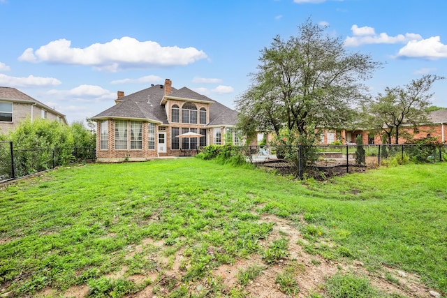 back of house featuring a lawn, brick siding, a chimney, and a fenced backyard