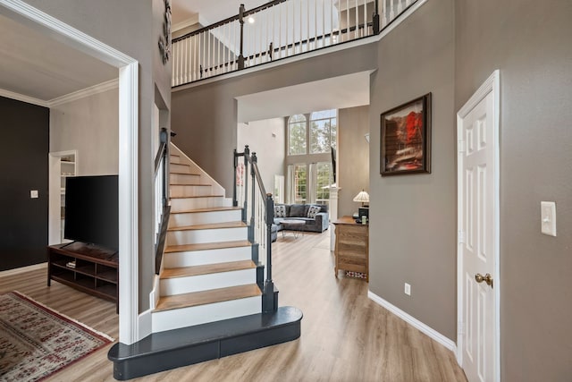 stairs featuring baseboards, ornamental molding, wood finished floors, and a towering ceiling