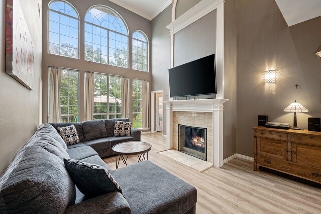 living area featuring crown molding, a high ceiling, a fireplace, light wood-style floors, and a healthy amount of sunlight