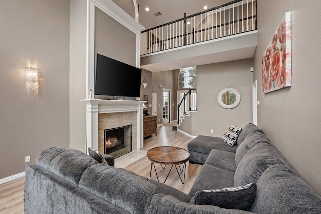 living room with visible vents, wood finished floors, a fireplace, baseboards, and a high ceiling