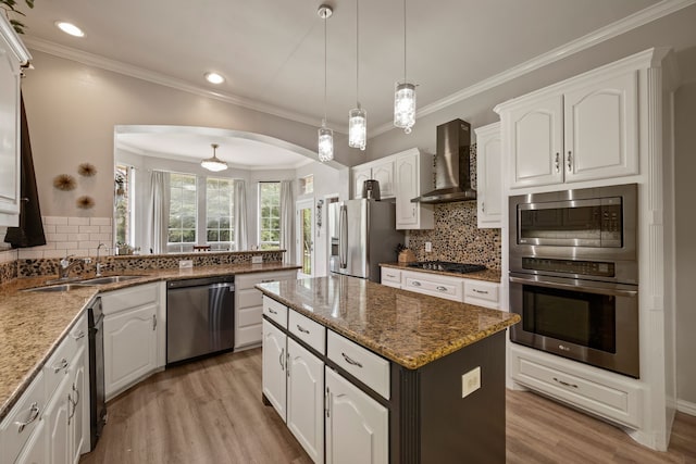 kitchen with appliances with stainless steel finishes, a sink, light wood finished floors, wall chimney exhaust hood, and a kitchen island