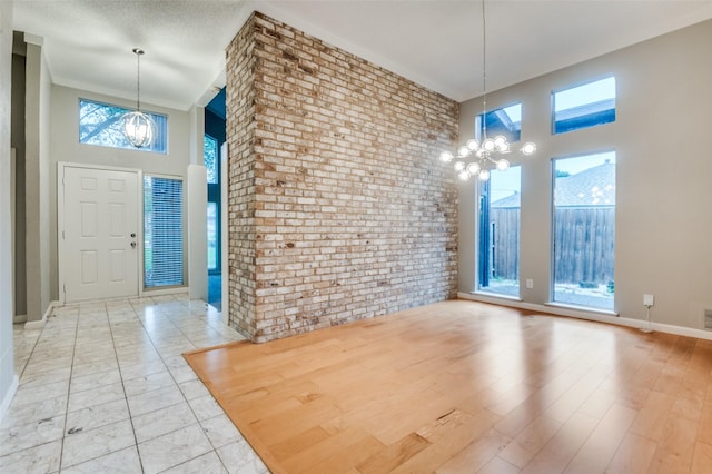 foyer featuring a chandelier, brick wall, a towering ceiling, and baseboards