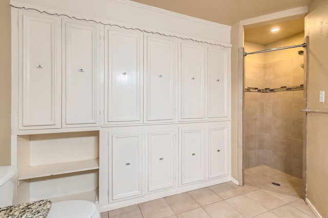 bathroom featuring baseboards, toilet, tile patterned floors, and tiled shower