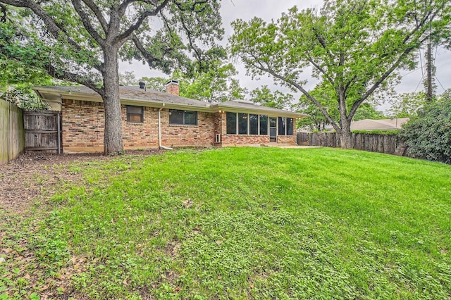 back of property with brick siding, a sunroom, a fenced backyard, a chimney, and a yard