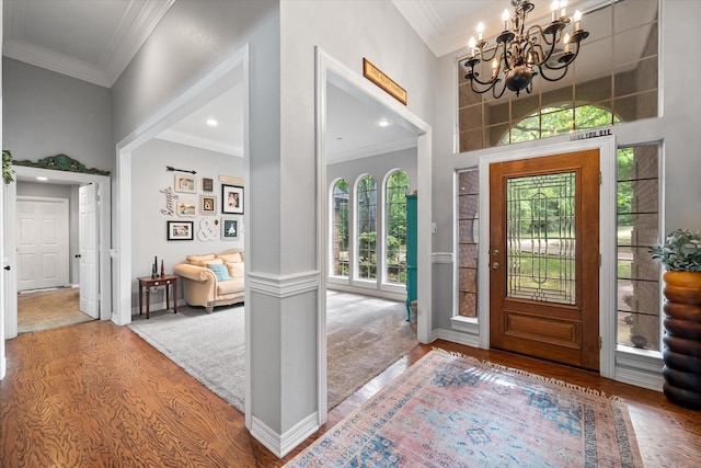 entryway featuring ornamental molding, a towering ceiling, wood finished floors, recessed lighting, and a notable chandelier
