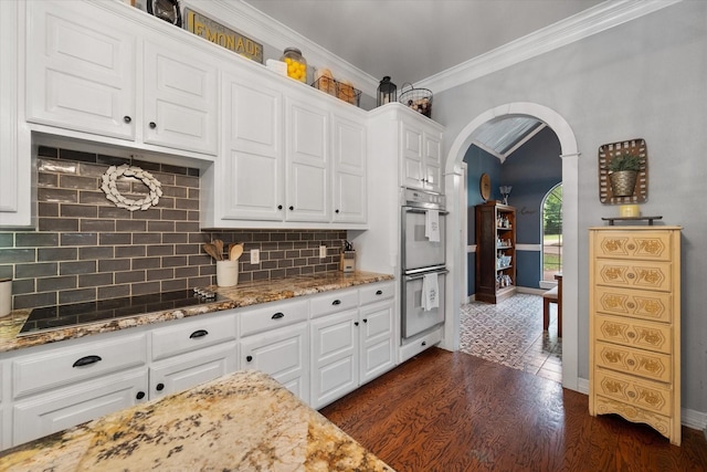 kitchen with crown molding, double oven, black electric stovetop, white cabinets, and arched walkways