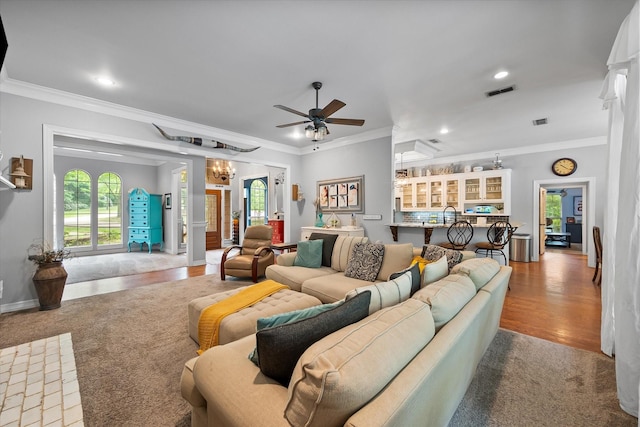 living area with crown molding, ceiling fan with notable chandelier, recessed lighting, baseboards, and visible vents