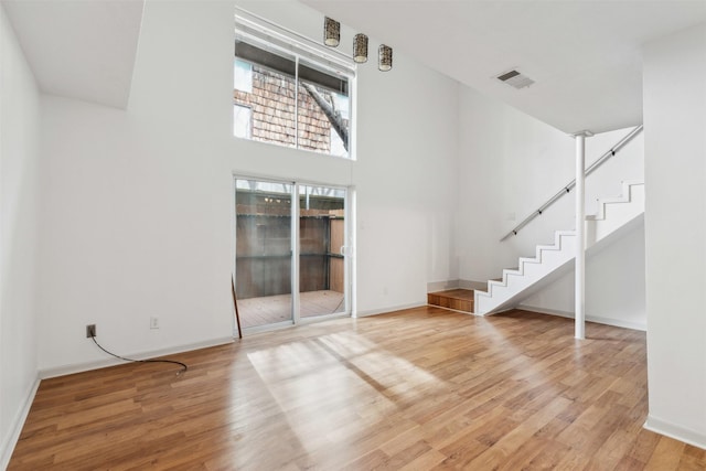 unfurnished living room with a high ceiling, baseboards, wood finished floors, visible vents, and stairway