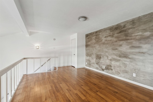 empty room featuring baseboards, lofted ceiling with beams, and wood finished floors