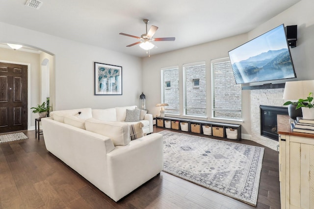 living room featuring visible vents, wood finished floors, a stone fireplace, arched walkways, and a ceiling fan