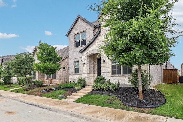 view of front of property featuring cooling unit, a front yard, brick siding, and stone siding