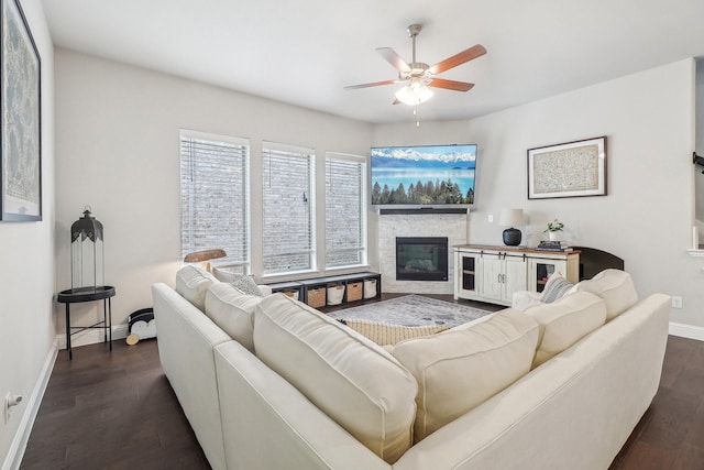 living area featuring baseboards, dark wood-style flooring, ceiling fan, and a fireplace