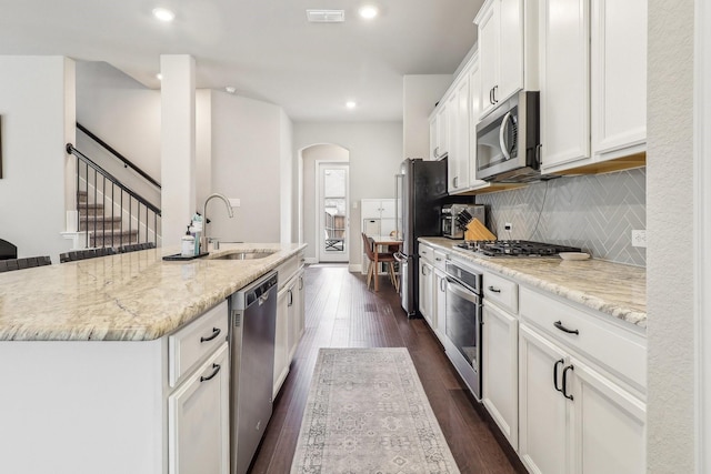 kitchen featuring arched walkways, a sink, stainless steel appliances, white cabinetry, and an island with sink