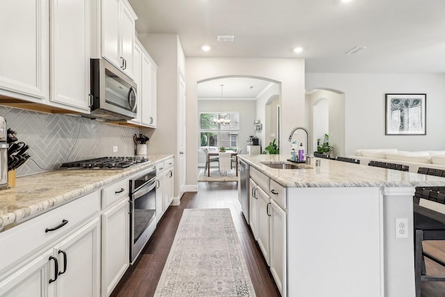 kitchen featuring white cabinets, appliances with stainless steel finishes, a sink, arched walkways, and an island with sink