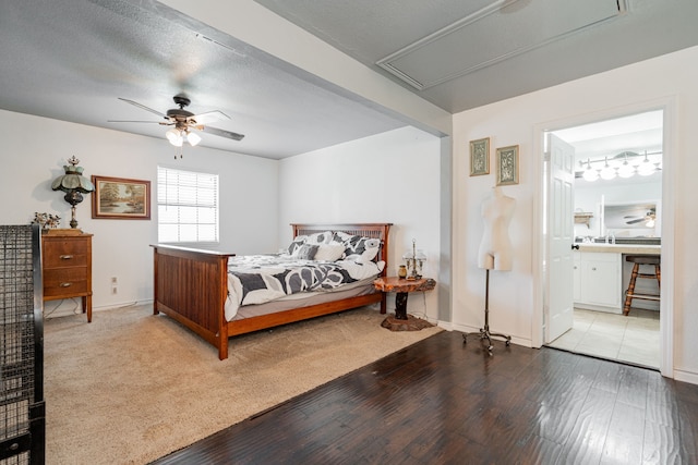 bedroom with connected bathroom, attic access, hardwood / wood-style floors, a ceiling fan, and baseboards