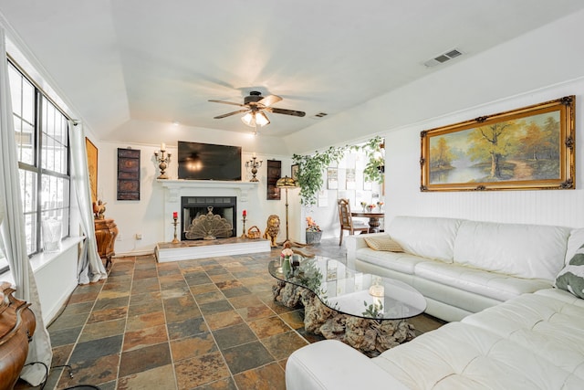 living area featuring stone finish floor, ceiling fan, a fireplace with raised hearth, and visible vents