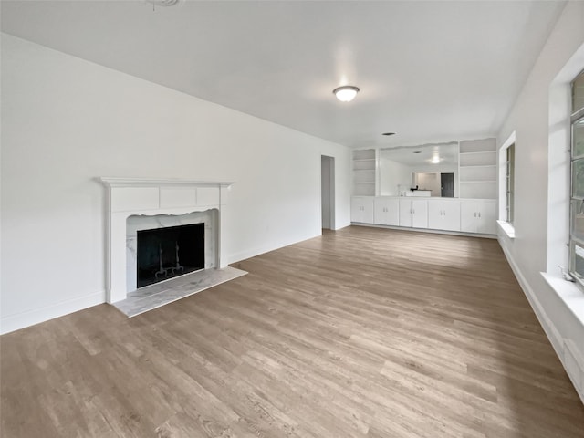 unfurnished living room with built in features, baseboards, wood finished floors, and a premium fireplace