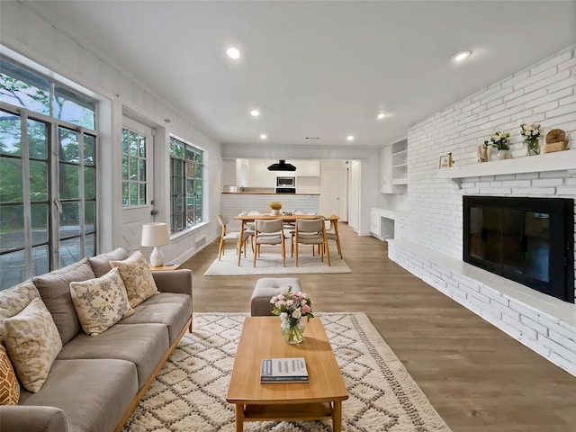 living area with brick wall, visible vents, a fireplace, wood finished floors, and recessed lighting