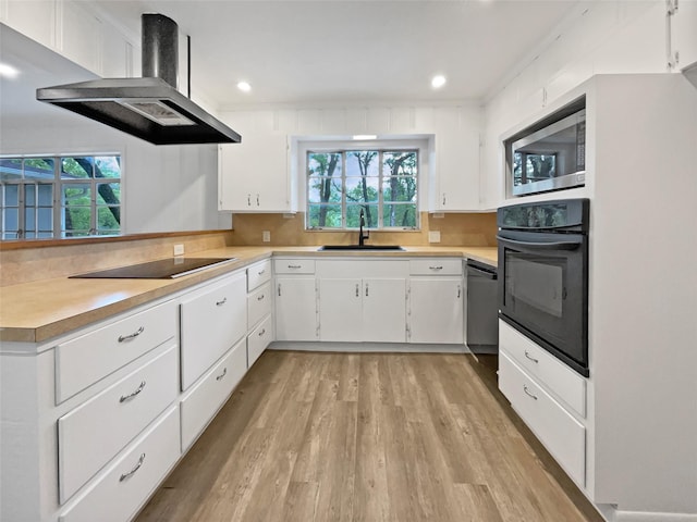 kitchen with a sink, black appliances, wall chimney exhaust hood, and a wealth of natural light