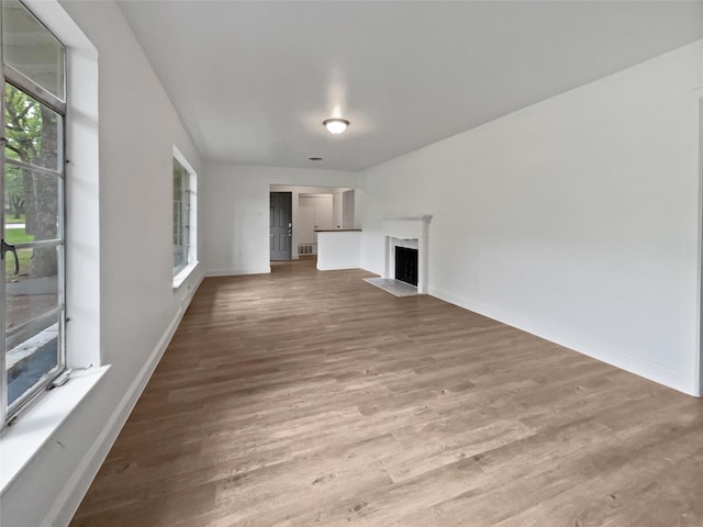 unfurnished living room featuring baseboards, a fireplace with flush hearth, and wood finished floors