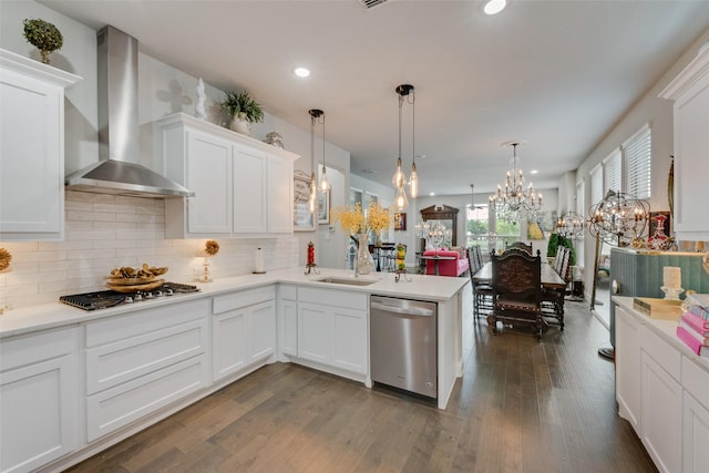 kitchen featuring white cabinets, light countertops, wall chimney exhaust hood, stainless steel appliances, and a peninsula