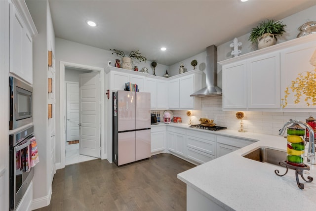 kitchen featuring wall chimney range hood, appliances with stainless steel finishes, a sink, white cabinetry, and backsplash