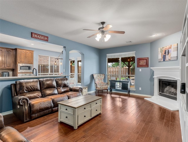 5732 Chateau Dr, Sachse, TX 75048 - living area featuring ceiling fan, arched walkways, dark wood-style floors, a fireplace with raised hearth, and baseboards
