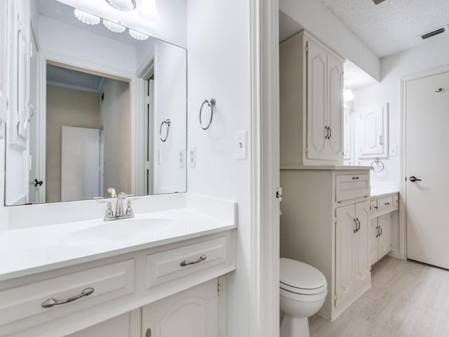 12203 Cross Creek Dr, Dallas, TX 75243 - bathroom with visible vents, vanity, wood finished floors, toilet, and a textured ceiling
