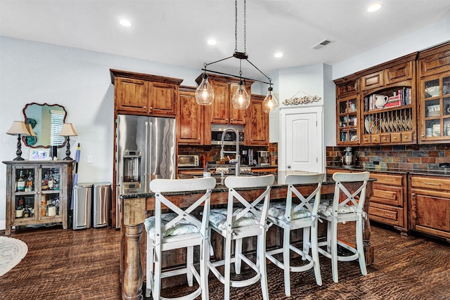 kitchen featuring a kitchen breakfast bar, an island with sink, stainless steel appliances, backsplash, and visible vents