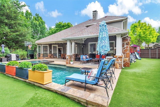 back of property with an in ground hot tub, a patio area, fence, a yard, and a shingled roof