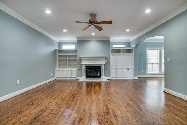 unfurnished living room with a ceiling fan, arched walkways, wood finished floors, a glass covered fireplace, and ornamental molding