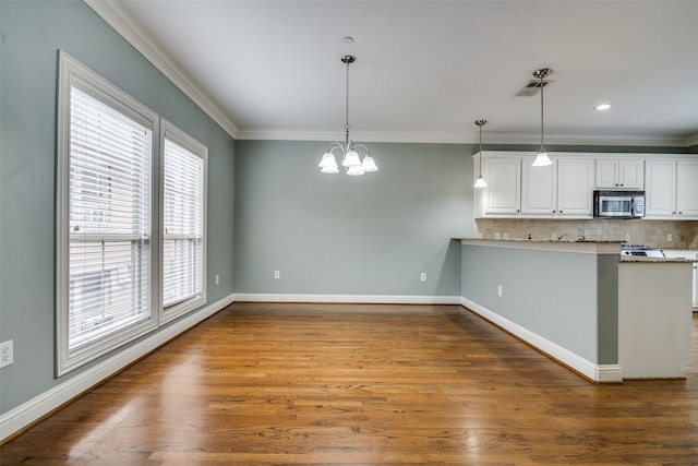 kitchen with decorative backsplash, white cabinets, stainless steel microwave, an inviting chandelier, and ornamental molding