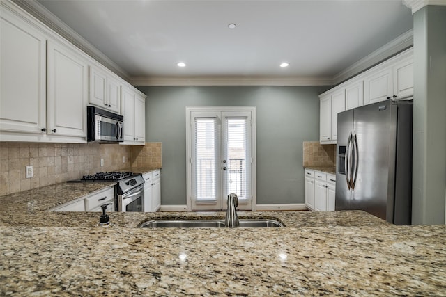 kitchen with a sink, light stone counters, white cabinets, ornamental molding, and stainless steel appliances