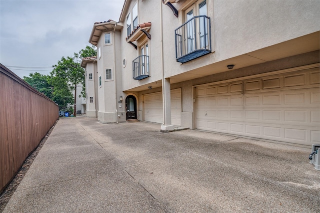 exterior space with fence, stucco siding, an attached garage, and driveway
