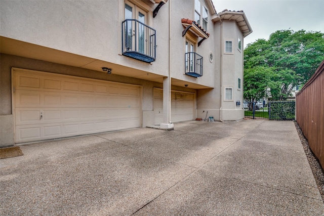 exterior space featuring fence, a garage, stucco siding, a balcony, and driveway