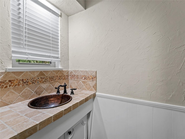 2345 Ravenwood Dr, Grand Prairie, TX 75050 - bathroom with vanity, a textured wall, decorative backsplash, and a wainscoted wall
