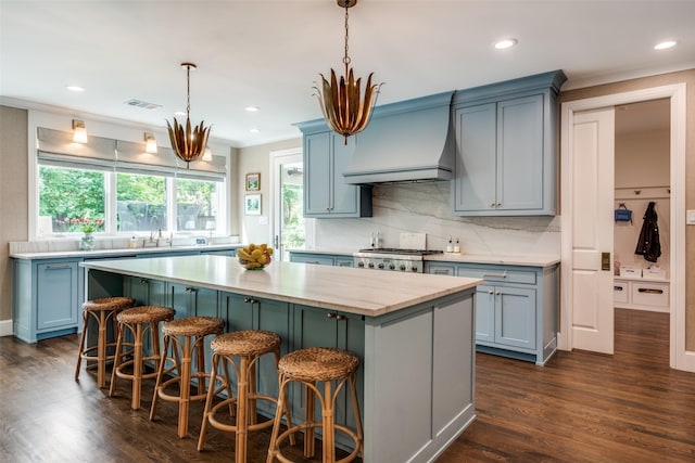kitchen featuring visible vents, a kitchen island, light countertops, custom range hood, and backsplash