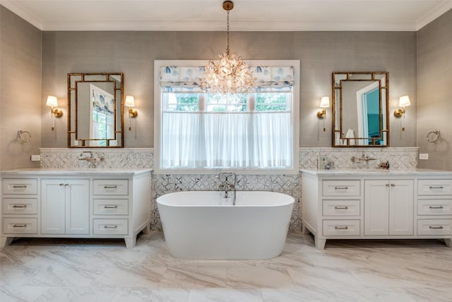 full bathroom with an inviting chandelier, a freestanding bath, a sink, two vanities, and ornamental molding