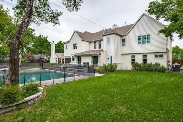 back of property with central AC, a fenced backyard, a chimney, a fenced in pool, and a lawn