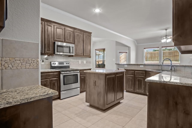 2217 Caroline Dr, Weatherford, TX 76087 - kitchen featuring appliances with stainless steel finishes, arched walkways, a sink, light stone counters, and ornamental molding