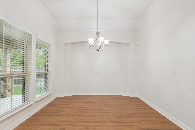 unfurnished dining area featuring baseboards, ornamental molding, wood finished floors, and a notable chandelier