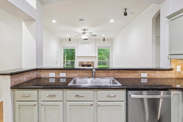 kitchen with a ceiling fan, backsplash, stainless steel dishwasher, a sink, and dark stone counters