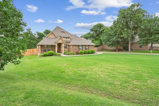 craftsman-style home featuring brick siding, a front lawn, roof with shingles, and fence